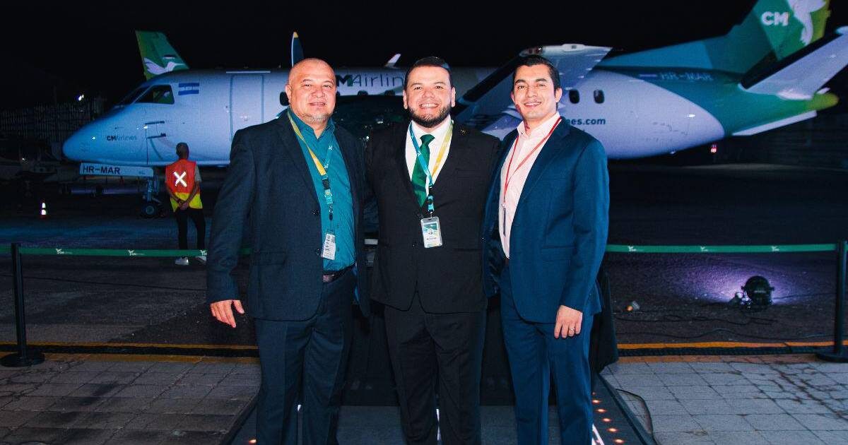Tres ejecutivos frente a un avión SAAB de CM Airlines durante el acto de lanzamiento, de noche en la plataforma del aeropuerto.